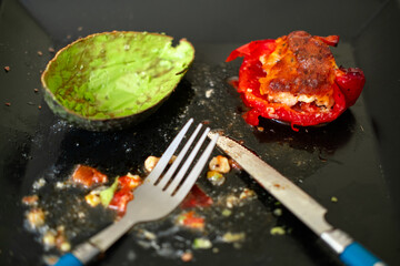 Empty plate with fork, knife, avocado half, and stuffed red pepper remnants.