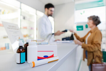 Selective focus on various medications on counter with senior woman customer buying it and paying with phone on background