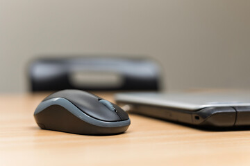 Wireless mouse and closed laptop on wooden table in business conference room with black plastic...