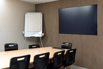 Modern conference room with table, chairs, flip chart and wall-mounted TV