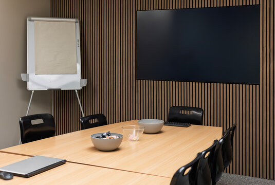 Modern business conference meeting room with table, chairs, flip chart and wall-mounted TV on modern wood panelled wall