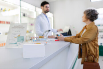 Obraz premium Selective focus on medication package with male pharmacist and senior woman talking at store counter for pharmaceutical advice and opinion of pharmacist