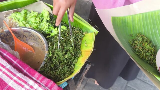A close-up of a person preparing Pecel Semanggi, a traditional Indonesian dish made of water clover, with a ladle to mix the ingredients.