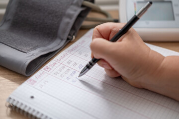 health daily tracking, hand writing blood pressure readings from monitor on sheet of paper, documenting blood pressure results, self-monitoring measurement, cardiovascular health