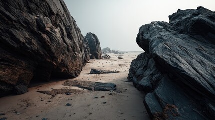 Fototapeta premium A rugged coastal landscape scene with large dark rocks and sand in a foggy atmosphere showcasing a natural shoreline with rugged geological formations