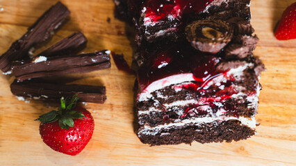 Rich chocolate cake decorated with elegant chocolate swirls and fresh strawberries on a wooden board. Perfect for dessert photography and bakery content