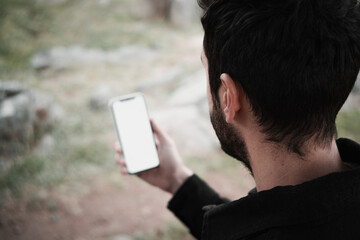 Close-up of a young man sitting in a park and using a smartphone. Copy and paste on cell phone...