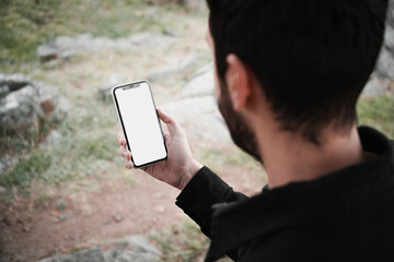 Close-up of a young man sitting in a park and using a smartphone. Copy and paste on cell phone...