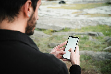 Close-up of a young man sitting in a park and using a smartphone. Copy and paste on cell phone...