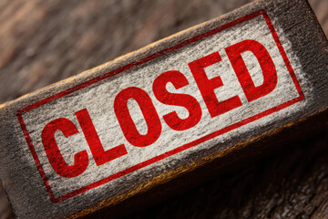 Red closed sign on a weathered wooden block with a distressed and rustic appearance close up view