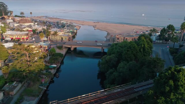 Aerial view of Capitola, California, USA, showing the beach, pier, and bridges over the Soquel Creek. Cars and people are crossing the bridges.
