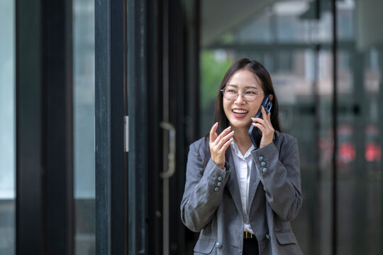 Businesswoman walking and talking on phone outside office building - Powered by Adobe
