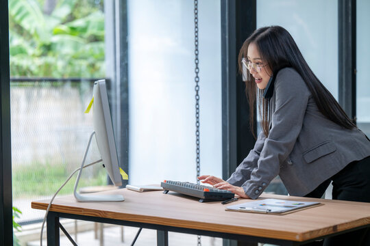 Businesswoman multitasking, typing and talking on phone in modern office