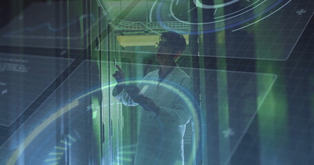 Pointing man wearing white lab coat checking server modules in data center, with HUD graphics