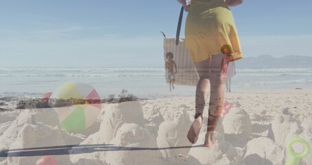 Mother and children walking and playing in oceanfront sand by surf, with sandcastles and beach ball