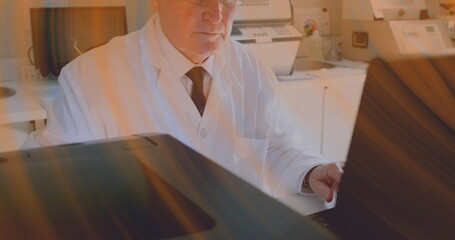 Working researcher wearing white lab coat typing on laptop at lab desk, with scanners and printers