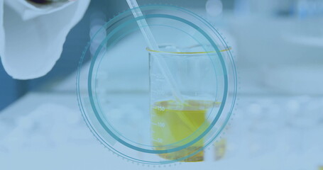 Pipetting yellow liquid into marked beaker on lab bench by gloved hand with circular overlay