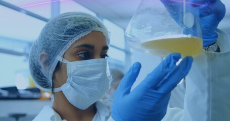 Inspecting lab technician wearing hairnet, mask, lab coat and gloves in lab, with Erlenmeyer flask