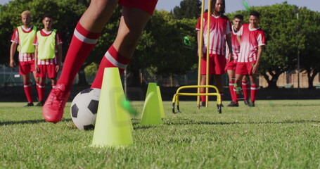 Legs in red cleats navigating black-and-white soccer ball through yellow drill cones on grass field