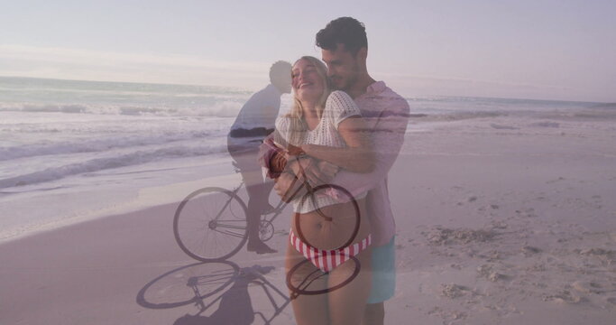 Embracing pregnant couple wearing striped bikini bottom on sandy beach, with bicycle silhouette