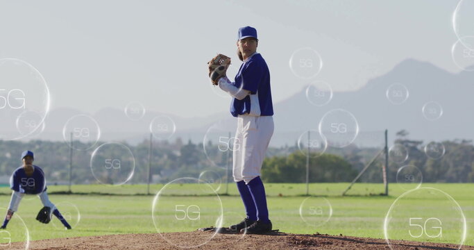 Pitching female baseball player gripping ball from clay mound at field, with floating 5G icons