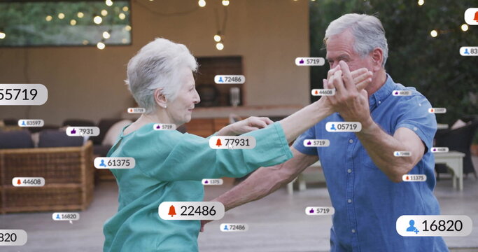 Dancing senior couple wearing turquoise blouse, blue shirt on patio, with floating social icons