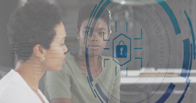Two women in office attire analyzing security HUD in office, with lock icon, circular interface