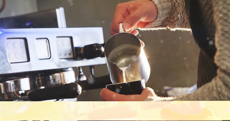 Barista hands wearing knit sweater pouring steamed milk into cup in cafe, with steel pitcher