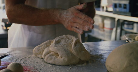 Pressing flour-covered hands kneading dough on steel worktable in bakery, with ingredient canisters