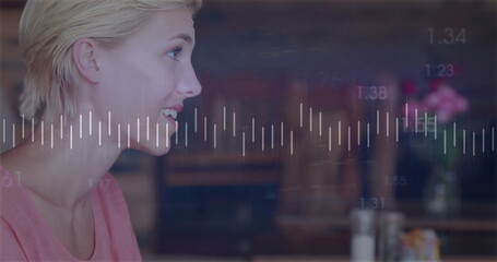 Sitting woman in pink top studying digital waveform in café, with numeric data, pink flower vase