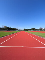 Empty running track stretches ahead, sunny skies, promoting athletic pursuits