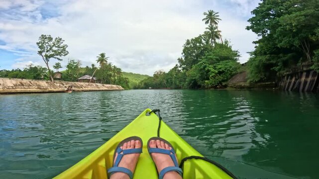 Kayaking down Lobok river with visible feet and tropical surroundings on Bohol island, Philippines Feet visible in kayak gliding through green waters of Lobok river on Bohol island, Philippines