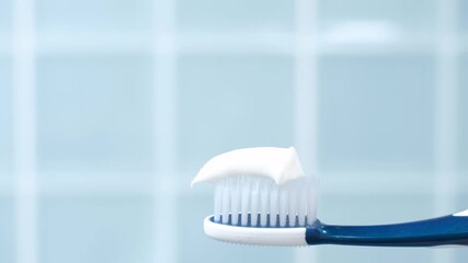 Female hand squeezing toothpaste onto toothbrush against blue tile background. - Powered by Adobe