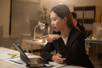 A woman in a black suit is pointing at something on a computer screen