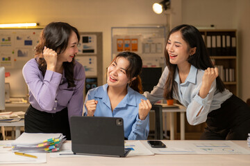 Three women are standing in front of a desk with a laptop