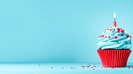 The cupcake, which is blue and has red sprinkles, also has a lit candle on it, all on a blue background