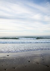 Obraz premium Pebbles on a Reflective Shore as Gentle Ocean Waves Roll In Under a Pale Sky