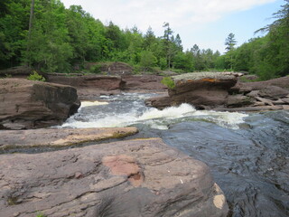 Top of Sandstone Falls along Whitewater River Edged by Brown Rocks and Surrounded by Green Forest Trees under Blue Sky with White Clouds