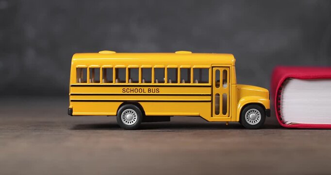 Toy yellow schoolbus driving into school book in front of chalkboard. Classic American public school bus traveling quickly towards a school textbook indicating excitement at going back to school.