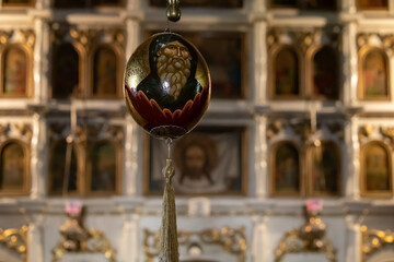 golden orthodox Easter egg with a saint's face, hanging inside a beautifully ornate church with gilded iconostasis in the background