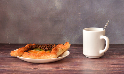 Layered pie with fruit jam, kiwi and tangerine slices decorated with coffee beans on a wooden table, a cup of hot coffee nearby.