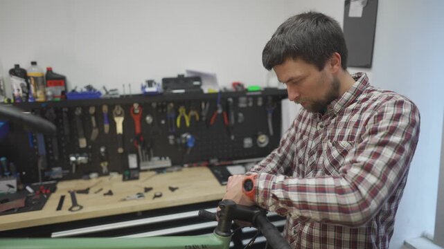 Bicycle mechanic wraps bicycle tape around handlebars of gravel bicycle at his workstation in cycle repair shop. Cycle engineer winding bike handlebar tape on gravel bike at job site in workshop. 