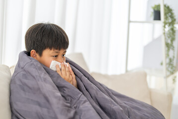 Young asian boy sneezing or blowing his nose and mouth with tissue, cold allergies or illness,...