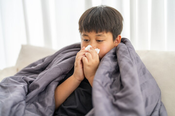 Young asian boy sneezing or blowing his nose and mouth with tissue, cold allergies or illness,...