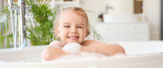 Cute little girl taking bath with foam and soap bubbles taking bath in bathroom