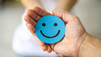 Hand holding blue paper cut happy smile face. Positive thinking, mental health assessment. World mental health day concept. Wellness and mental health. Detailed high quality image.