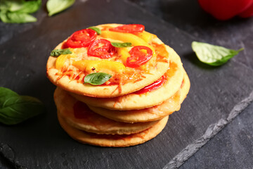 Board with tasty mini pizzas on black background