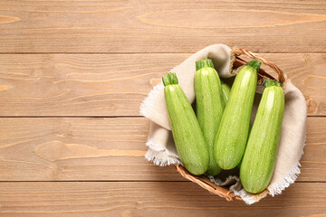 Wicker basket with many fresh green zucchini on wooden background