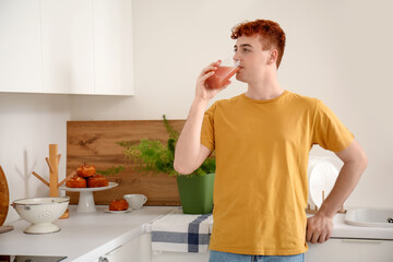 Young redhead man drinking juice in kitchen