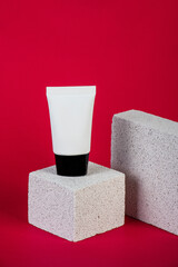 Plastic white tube for cream or lotion. Skin care or sunscreen cosmetic with stylish props on red background.